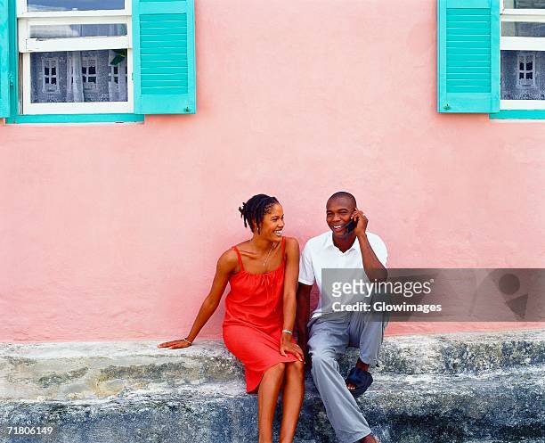 young couple sitting in front of a house and talking on a mobile phone, bermuda - bermudas imagens e fotografias de stock