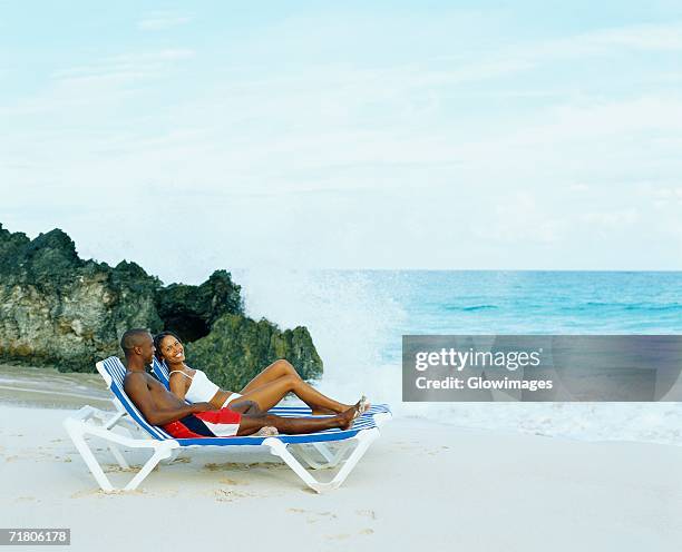 side profile of a young couple lying on lounge chairs on the beach, bermuda - bermuda beach stock-fotos und bilder