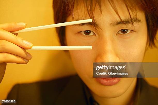 close-up of a young man holding chopsticks - holding chopsticks stock pictures, royalty-free photos & images