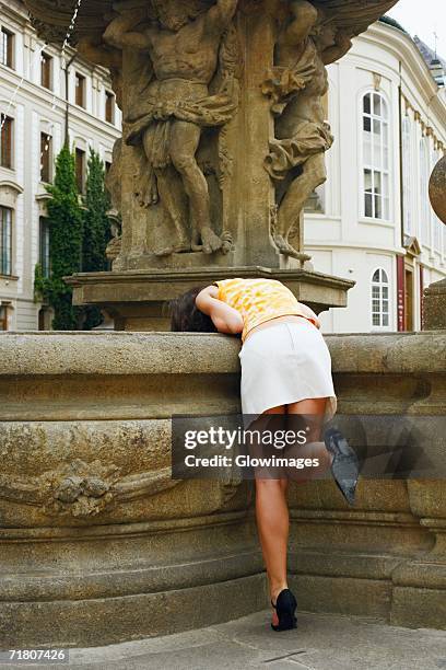 rear view of a woman bending over a fountain - bending over in skirt stock-fotos und bilder