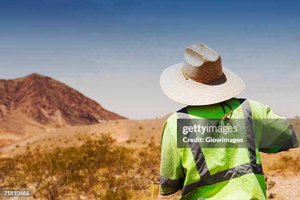 rear view of a construction worker standing at a construction site - sun hat stock pictures, royalty-free photos & images