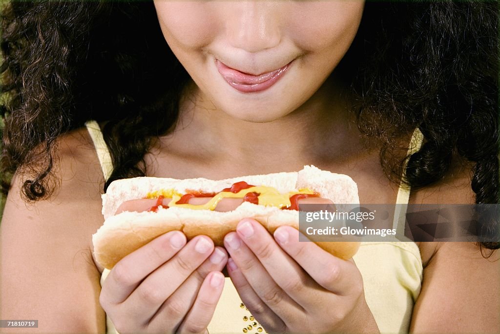 Close-up of a girl holding a hot dog and sticking her tongue out