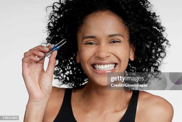 portrait of a young woman holding a pair of eyebrow tweezers - eyebrow tweezers stock pictures, royalty-free photos & images