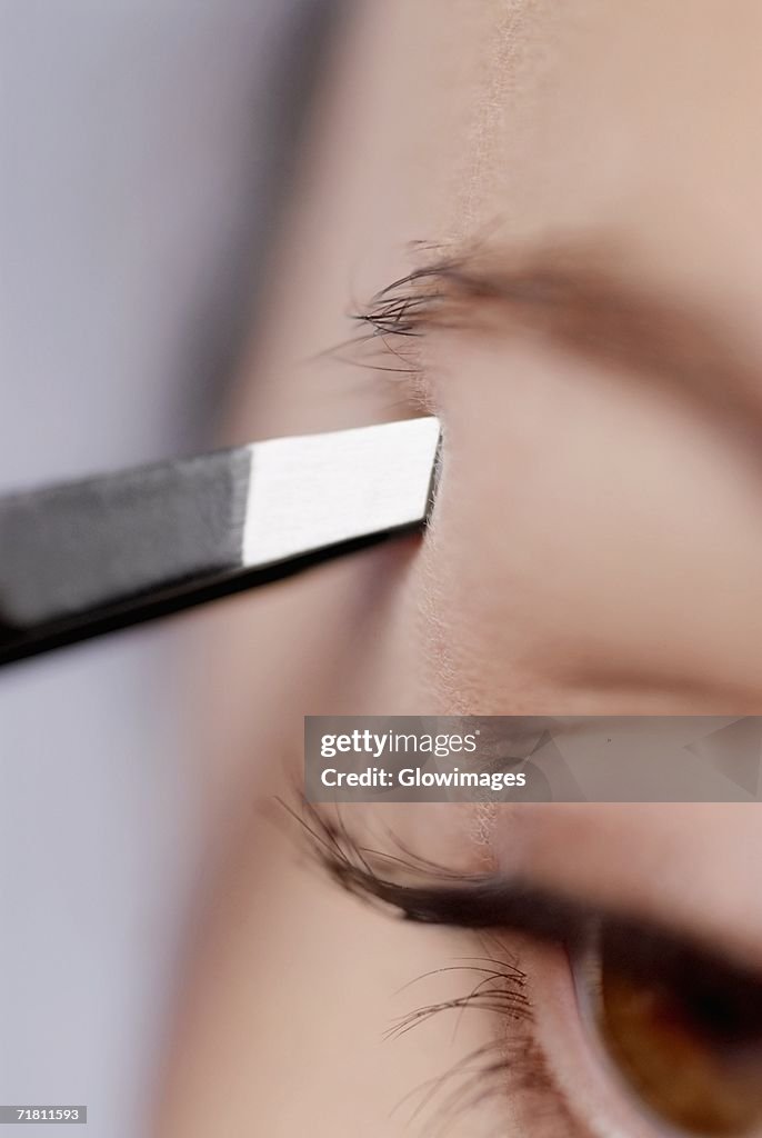 Close-up of a young woman tweezing her eyebrow