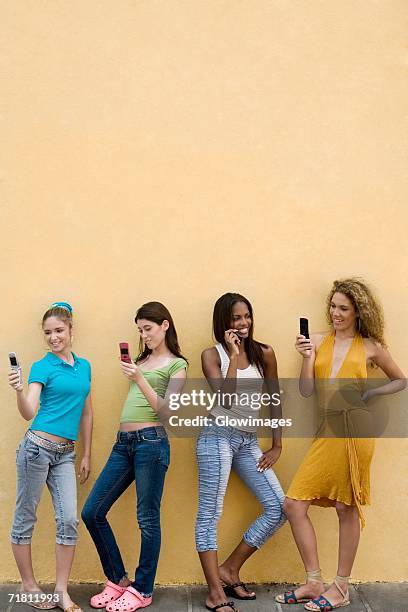 four teenage girls using mobile phones and smiling - feature phone stockfoto's en -beelden