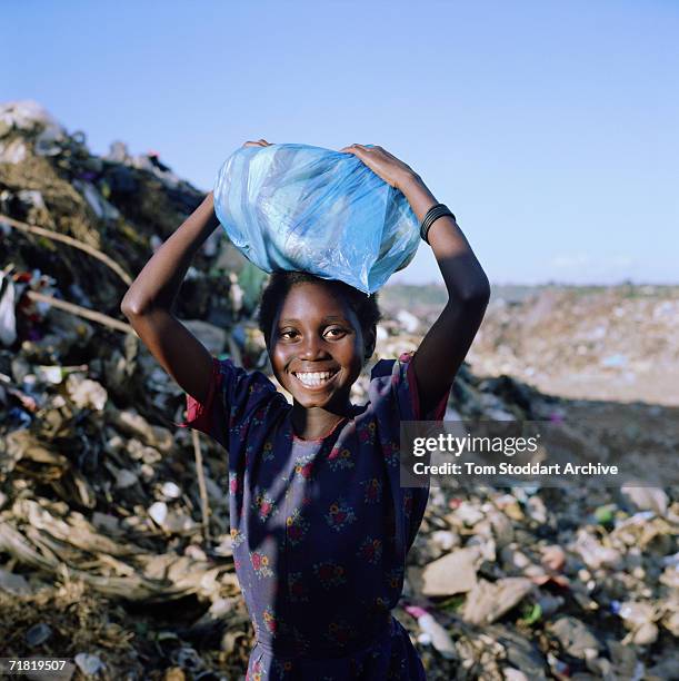 Smiling girl collecting plastic bags and bottles on a rubbish dump near Lusaka, Zambia, July 2002. Many of Zambia's poor scrape a living by...