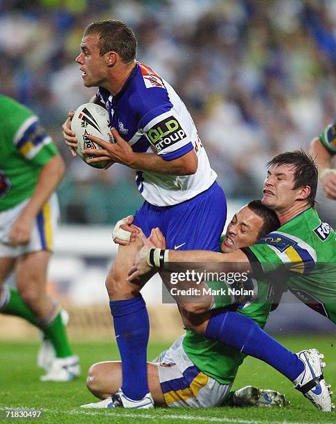 Daniel Holdsworth of the Bulldogs is tackled by Lincoln Withers and Kris Kahler of the Raiders during the NRL Third Qualifying Final between the...