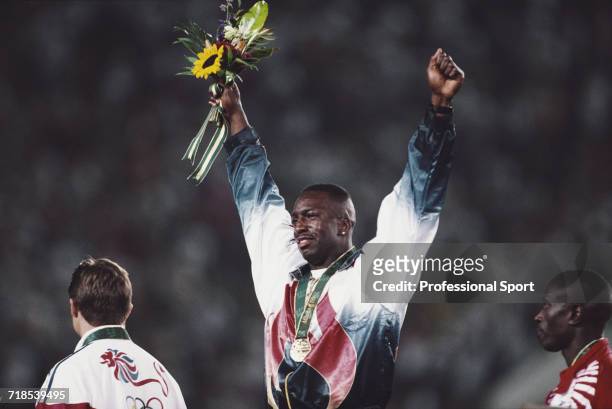 American athlete Michael Johnson raises his arms in the air in celebration on the medal podium after finishing in first place with an Olympic record...