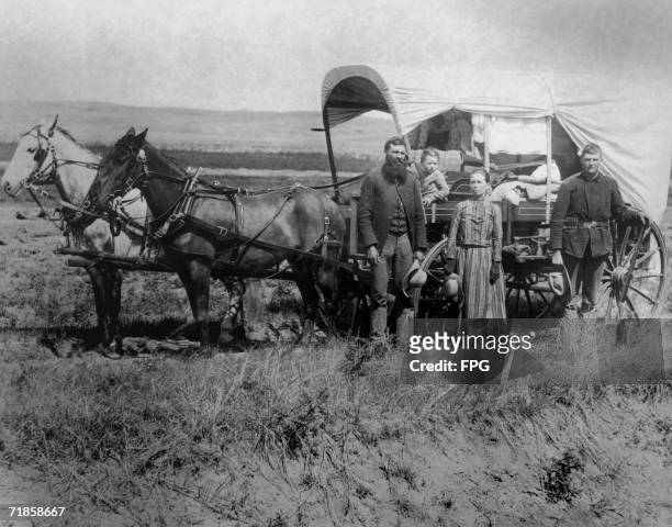 Family of pioneer settlers pose next to their covered wagon, 1886.