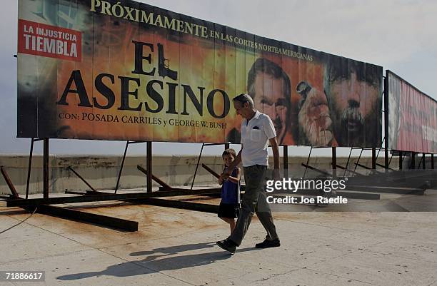 People walk past a billboard along the Malecon that reads "Coming Soon to North American Courts, The Assassin, with Posada Carriles and George W....