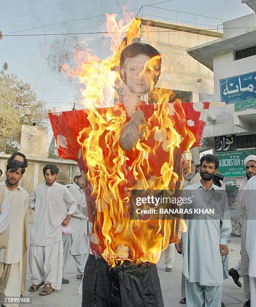 Pakistani activists from Jamaat-e-Islami look at a burning effigy of President Pervez Musharraf, during a protest against the killing of rebel tribal...