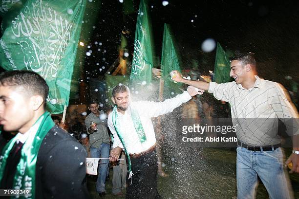 Palestinian youth sprays grooms that are seen wearing Hamas insignia green scarves as they line up during a mass wedding party organized by the...