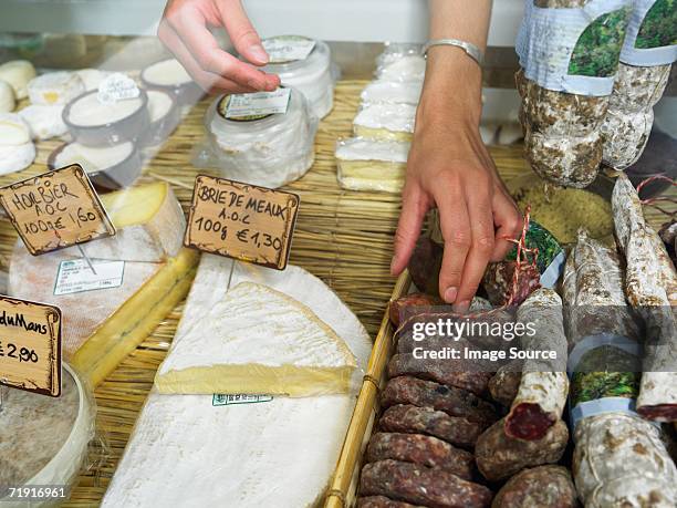 woman reaching into delicatessen display - french cheese stock pictures, royalty-free photos & images