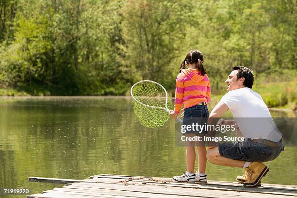 father crouching next to daughter on jetty, holding fishing net - girl with brown hair stock pictures, royalty-free photos & images