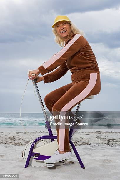 senior adult woman riding an exercise bike - tracksuit fotografías e imágenes de stock
