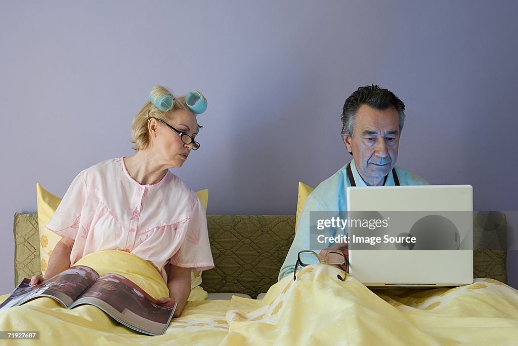 Couple in bed with laptop and magazine