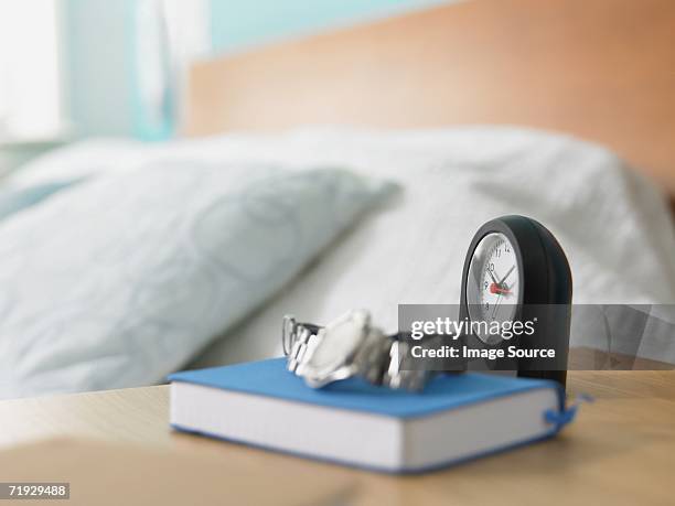 clock and book on a bedside table - bedside table stock pictures, royalty-free photos & images