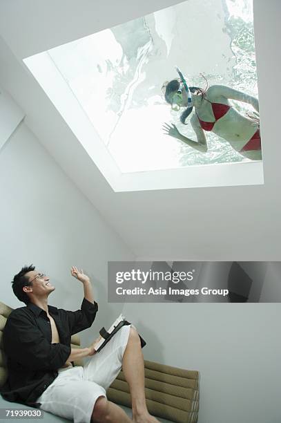 man in living room, waving at woman in swimming pool through the skylight - bermuda snorkel stock pictures, royalty-free photos & images