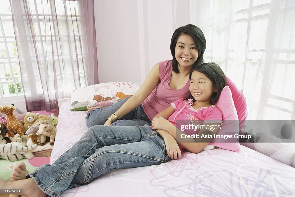 Mother and daughter in bedroom, side by side, looking at camera