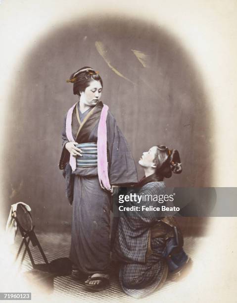 One Japanese woman helps another put on her obi or girdle, circa 1865.