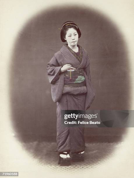 Japanese woman in a padded winter kimono and embroidered obi or sash, circa 1865.