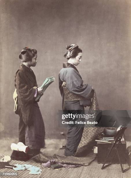 Japanese woman gets dressed, winding the long obi or sash around her waist, circa 1865.