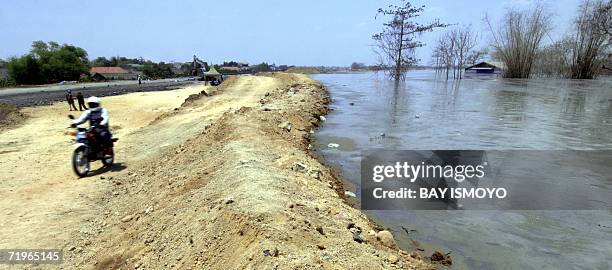 Motorcyclist rides past a dyke which is attempting to hold back the mud gushing out of a Lapindo Brantas Inc. Gas exploration well in Sidoarjo, East...