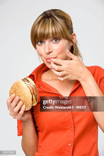 young woman licking finger, holding hamburger, portrait, close-up - 指をくわえる ストックフォトと画像