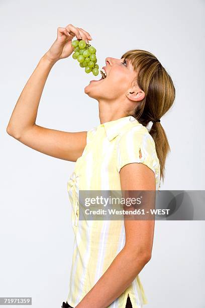 young woman holding bunch of grapes to mouth, profile, close-up - mouth open profile stock pictures, royalty-free photos & images