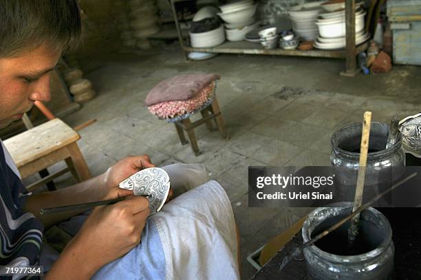 An Uzbek potter paints traditional patterns on a plate before it is glazed andf fired in a workshop, making the blue ceramics that the region is...