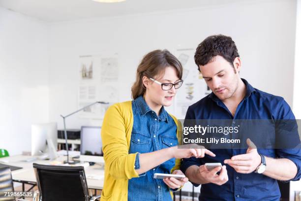 colleagues in office looking down discussing smartphones - phone comparison stock pictures, royalty-free photos & images