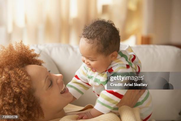 african mother and baby smiling at each other on sofa - black mother holding newborn stock-fotos und bilder