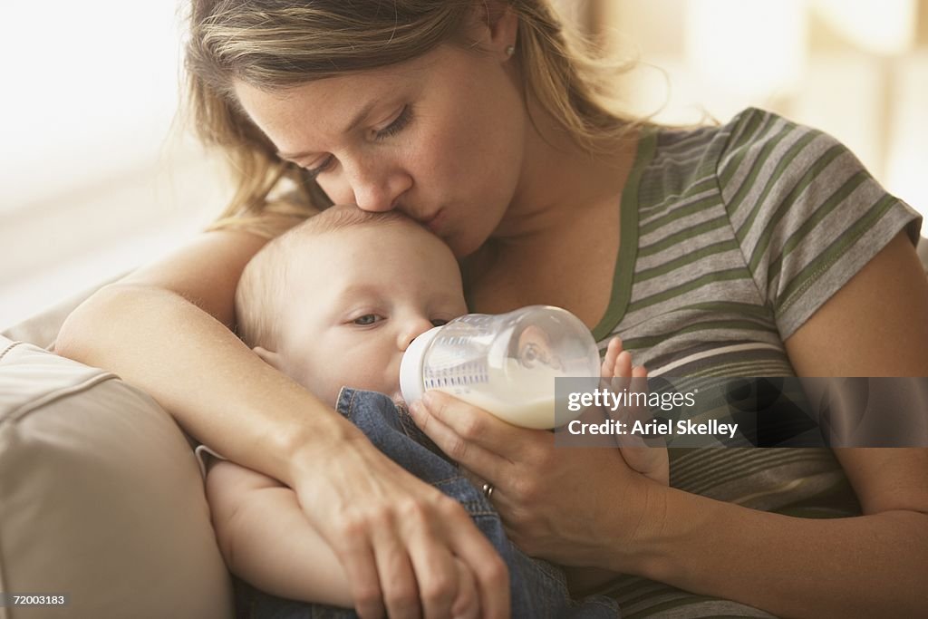 Mother feeding baby with bottle on sofa