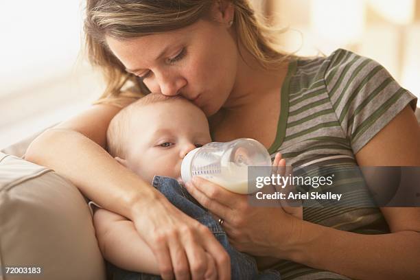 mother feeding baby with bottle on sofa - feeding baby stock pictures, royalty-free photos & images