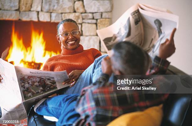 senior african couple with newspapers on sofa - zeitung lesen zwei personen stock-fotos und bilder