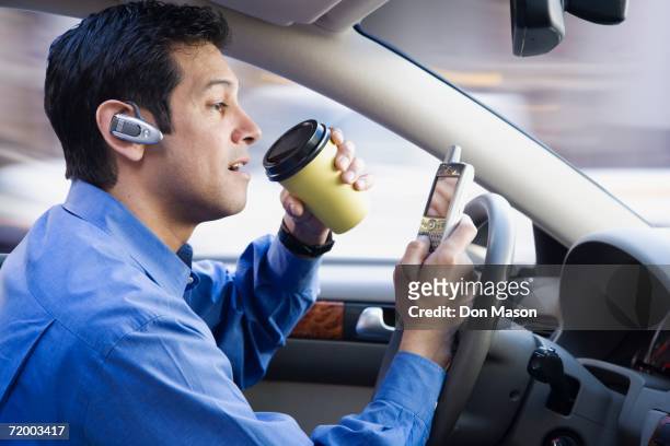 hispanic businessman using cell phone drinking coffee and driving - distracted driving stock pictures, royalty-free photos & images