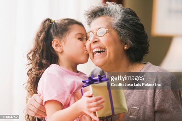 hispanic granddaughter kissing grandmother and holding gift - child giving gift ストックフォトと画像