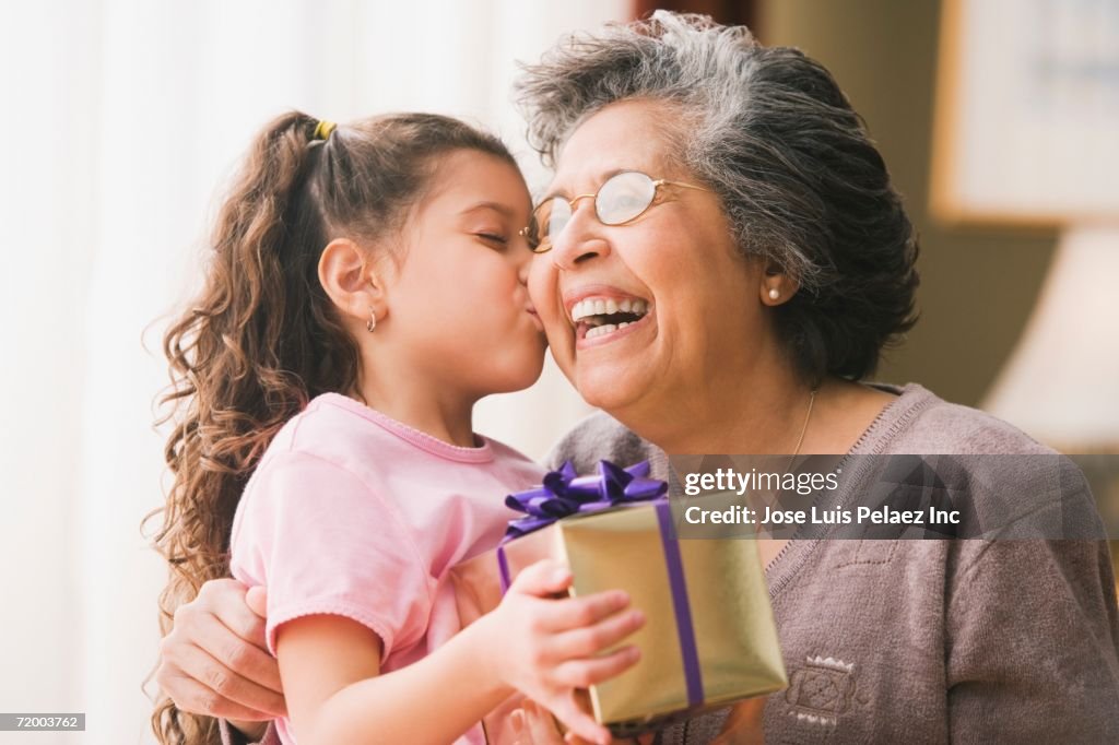 Hispanic granddaughter kissing grandmother and holding gift