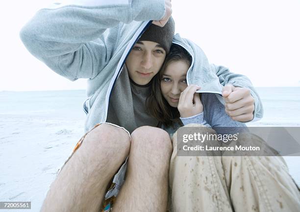 couple covering heads with jacket in the rain, on beach - wet sweatshirt fotografías e imágenes de stock