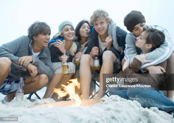 group of young adults sitting around beach campfire, with bottles of beer - kiss of fire stock pictures, royalty-free photos & images