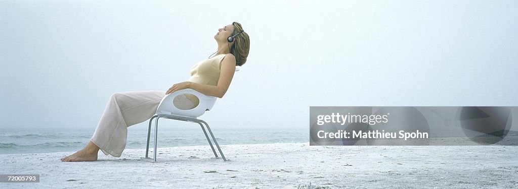 Woman sitting in chair on beach, wearing headphones