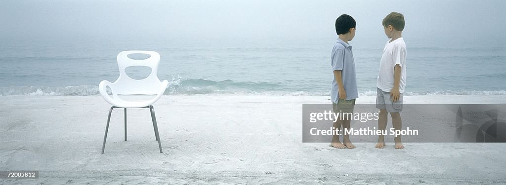 Two boys standing on beach, looking over shoulders at ocean
