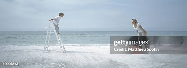 on beach, boy standing on ladder facing woman standing on sand, both screaming - vornüber beugen stock-fotos und bilder