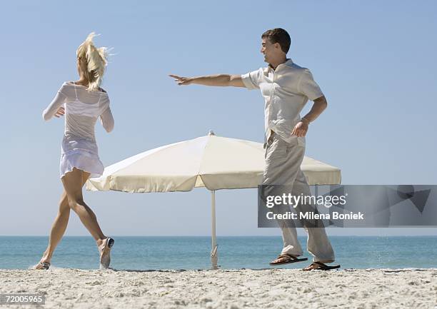 couple chasing each other around parasol on beach - seduzione foto e immagini stock