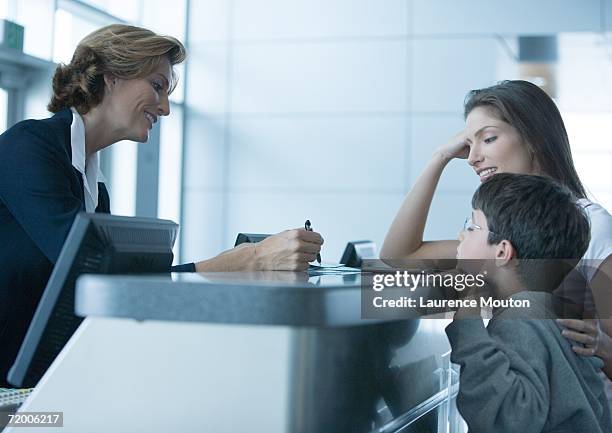 woman and son standing at check-in counter in airport - check in person stock pictures, royalty-free photos & images