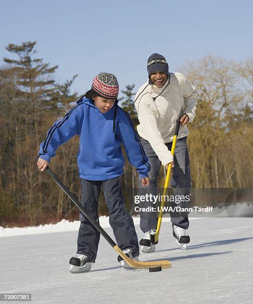 african father and son playing ice hockey - freeze motion stock-fotos und bilder