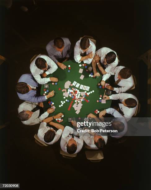 Overhead view of a large group of men as they crowd around a table for game of a poker variant called Texas Hold 'Em, August 1968.