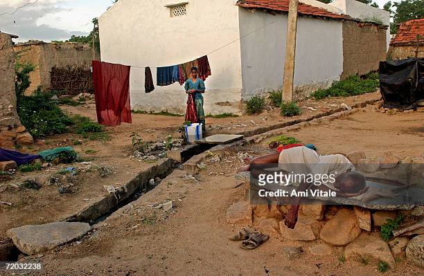 Dalit man sleeps in a village in Mehbubnagar district, in Andhra Pradesh, India while a young girl washes in this photo taken on August 22, 2005....