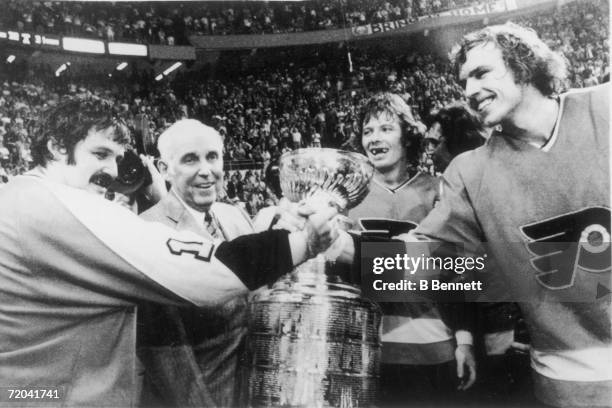 Canadian hockey players Bernie Parent and Bill Clement of the Philadelphia Flyers clasp hands as National Hockey League President Clarence Campbell...