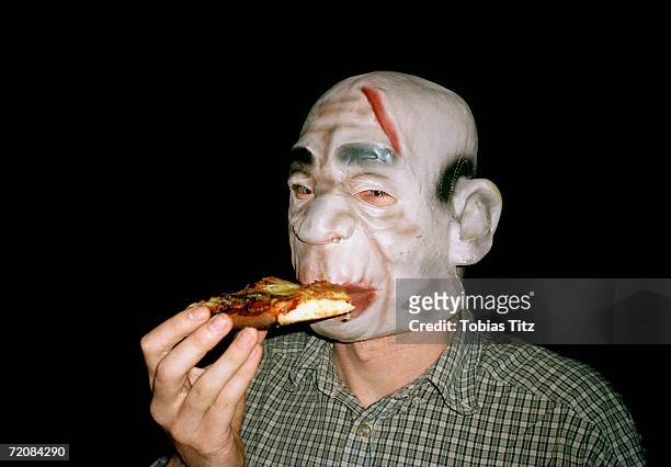 man wearing rubber monster mask and eating pizza - funny mask stockfoto's en -beelden